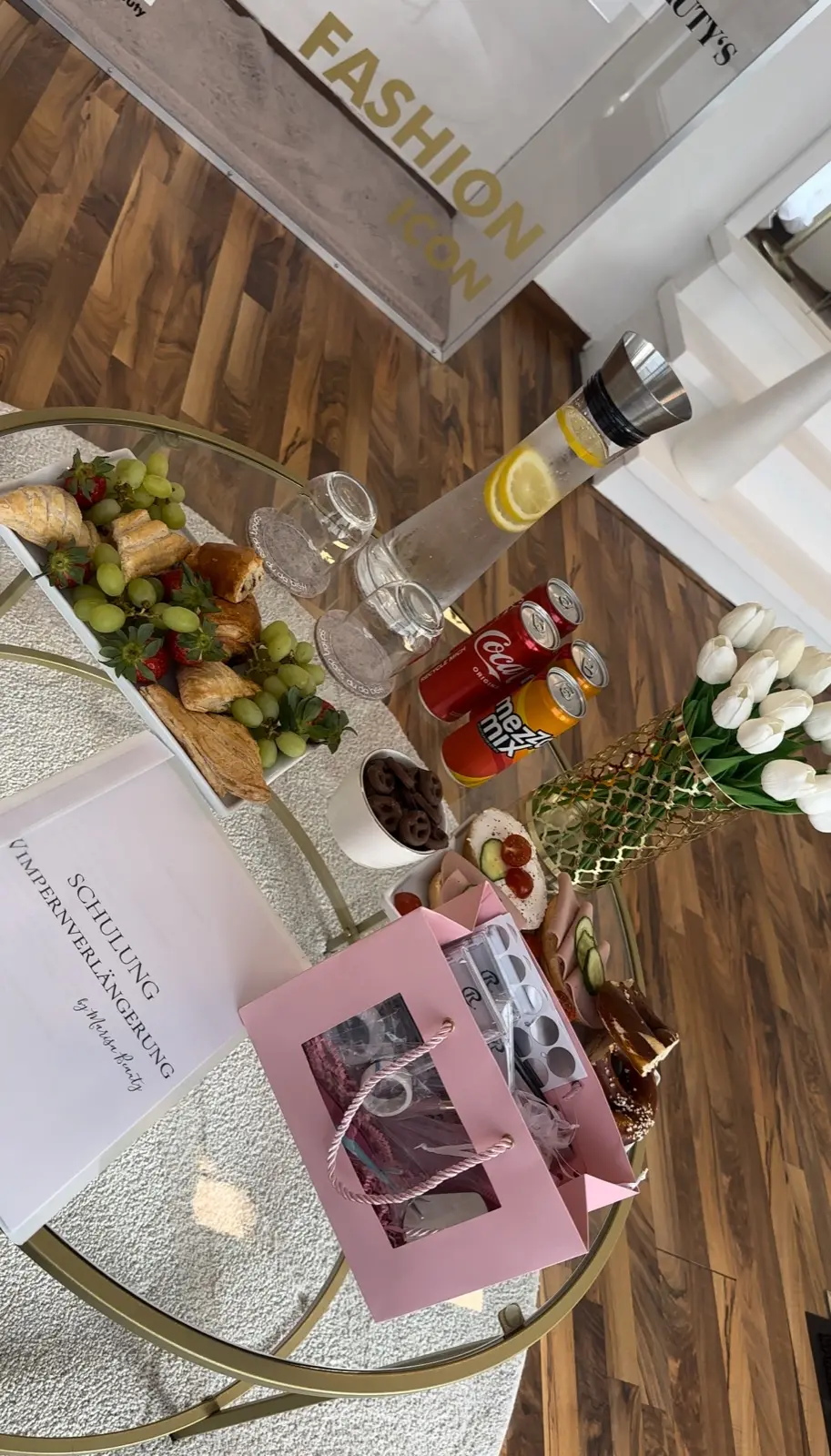 Gedeckter Glastisch mit Snacks, Getränken und rosa Goodie-Bag zur Wimpern-Schulung bei Marisa Beauty
